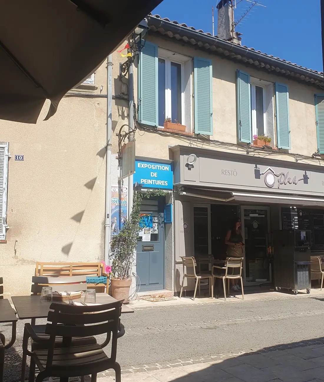 La façade d'Ô Plan : bandeau gris avec le logo et le mot Restô, volets céladon, chaises en terrasse