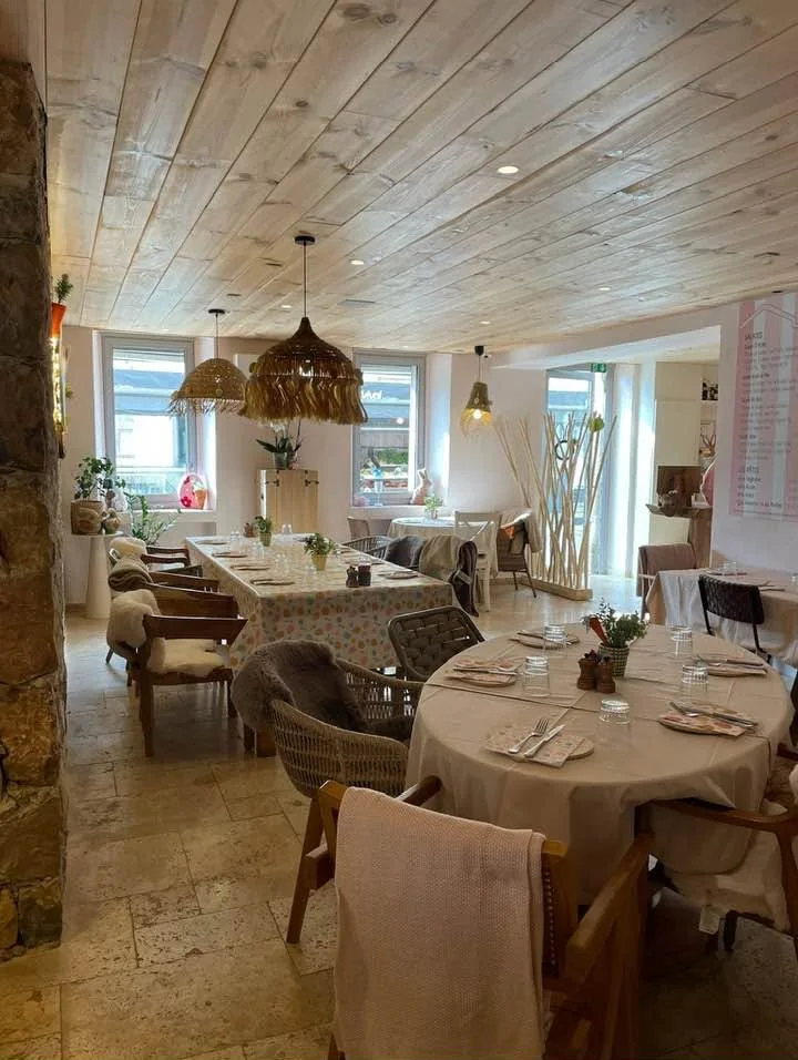 Salle lumineuse au plafond de bois : tables rondes nappées, fauteuils, suspensions en raphia