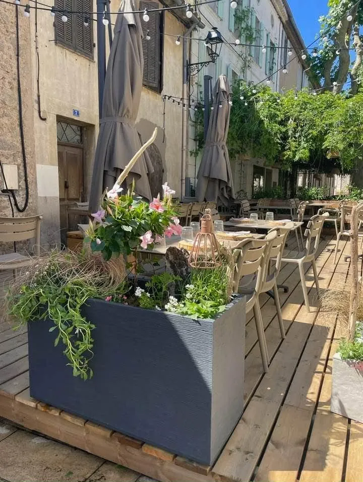 La terrasse sur plancher de bois : bacs fleuris, tables dressées, façades de pierre du village